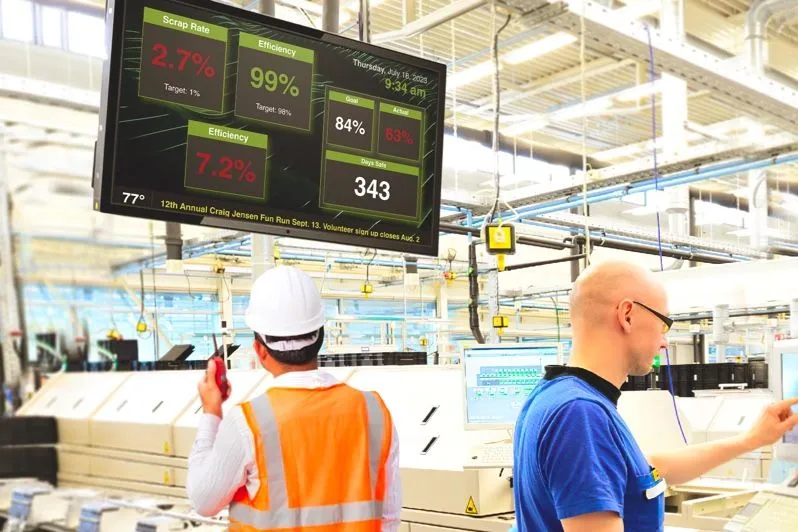 Ouvriers d’usine sous un écran affichant des chiffres de production