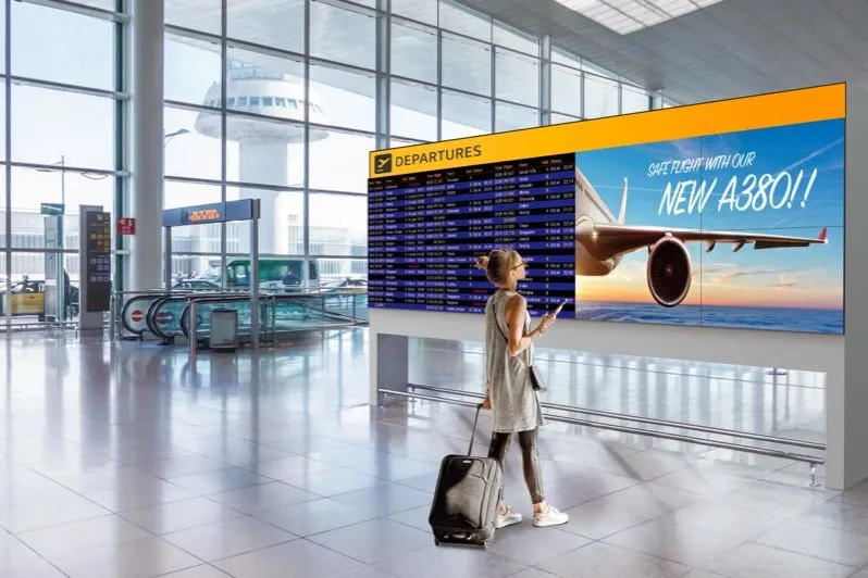 Voyageur avec une valise devant un tableau des départs dans un aéroport
